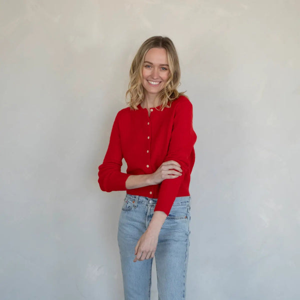 Woman wearing a red sweater and light blue jeans against a plain background
