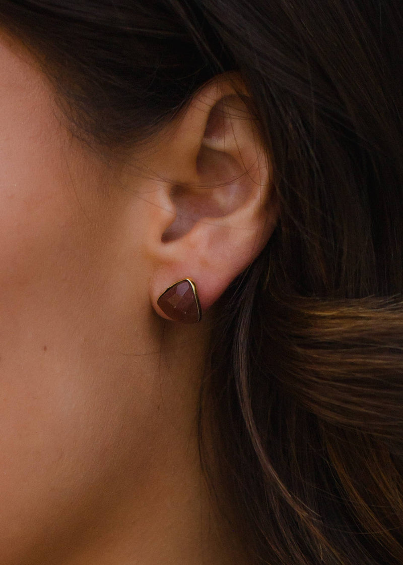 front view of the model wearing the red stud earring. shows the texture on it and that it has gold around it. 