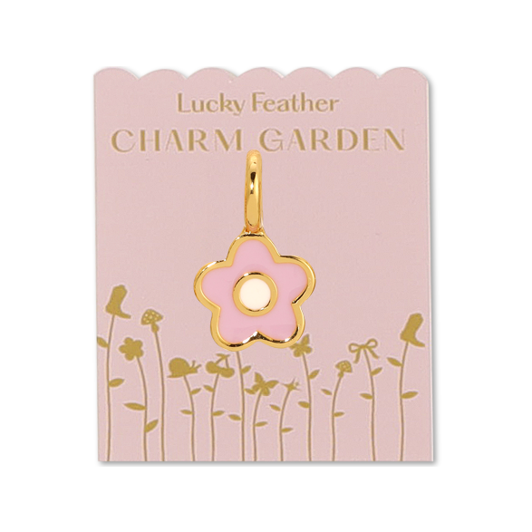 Front view of the gold flower charm on packaging. Shows the pink packaging with the gold words saying " LUCKY FEATHER CHARM GARDEN", also has gold flowers on the packaging as well. In the middle shows the gold flower charm that is pink with a white center. 