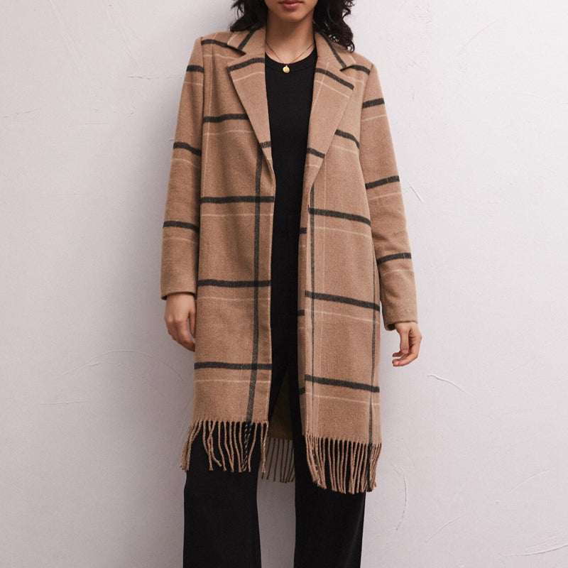 Front view of model wearing coat. Shows the on-seam pockets. Also shows the fringe detail at the bottom, the collar, the mid length and the black, brown and white plaid. 