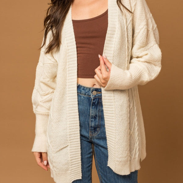 Front view of model wearing cardigan. Shows the open front. Also shows the mid thigh length and the tighter fitted cuffs on the sleeves. 