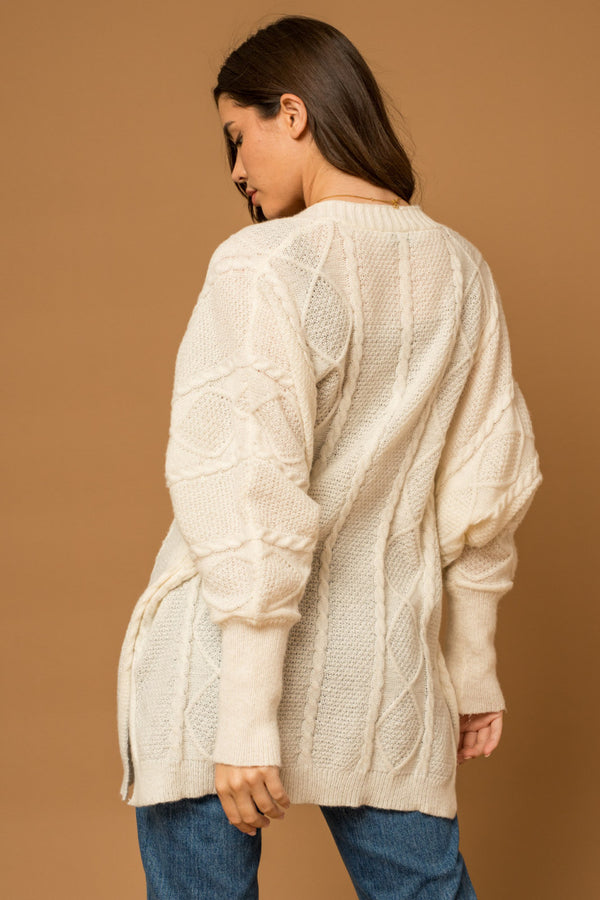 Back view of model wearing cardigan. Shows lmid tight length. Also shows the cable knit detail and the tight fitted cuff on the sleeves. 