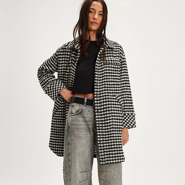 Person wearing a black and white checkered coat, black top, gray jeans, and black boots on a white background