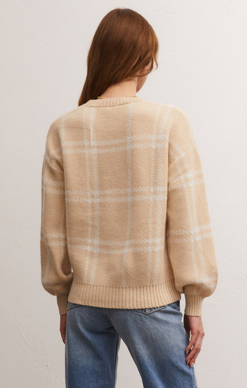 Back view of model wearing sweater. Shows the ribbed detailing on the neckline, cuffs and hem. Also shows that the sleeves are slightly puffy and that the sweater is relaxed fit. The color of the sweater is almond with the plaid pattern being white.
