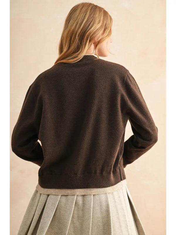 Person wearing a brown sweater and light-colored skirt against a beige background