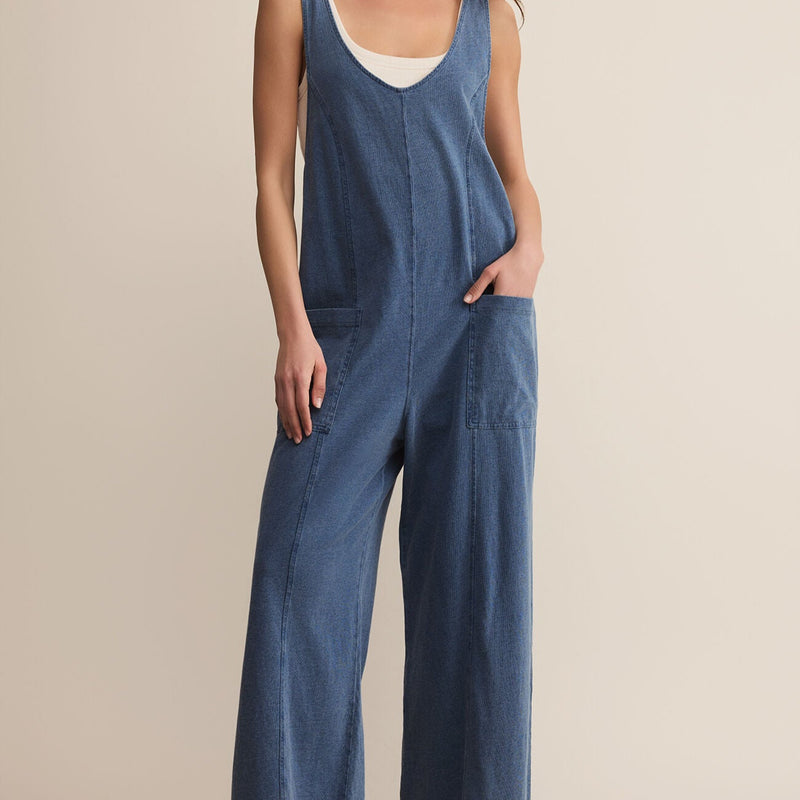 front view of the model wearing the everyday jersey denim jumpsuit. shows the scoop neckline. the wide leg, the blue coloring the front patch pockets, and the defined seaming. 