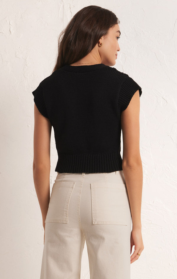 back view of the model wearing the roped in sweater vest. shows the slight cap sleeves. also shows the fitted style, the crop length of the sweater and that it sits right above the waist. 
