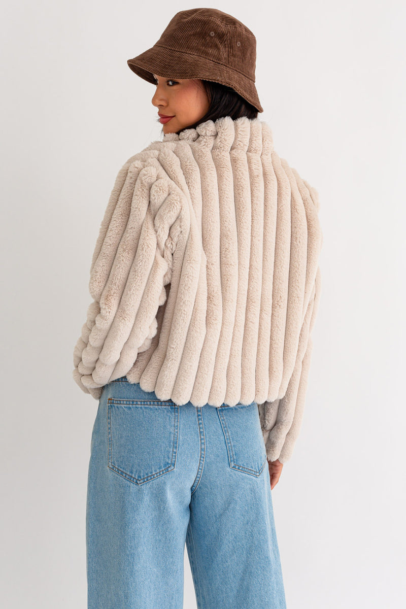 Back view of the model wearing the jacket. Shows the thick ribbing throughout. Also shows the crop length of the jacket, the fur texture and the beautiful cream color. 
