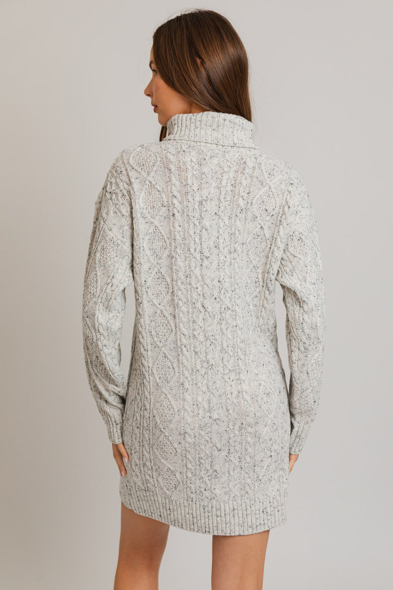 Back view of model wearing dress. Shows the cable knit detail. Also shows the turtleneck, the ribbed detail on the turtleneck, cuff and bottom hem. Shows the speckling in the fabric.