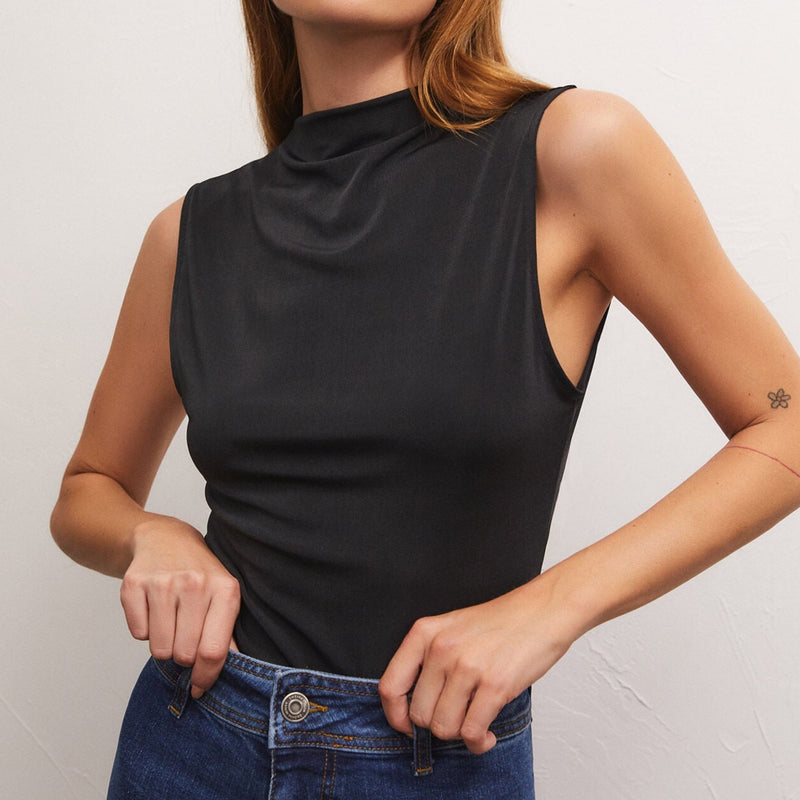 front view of model wearing the libra shine jersey top in black. shows the faux mock neckline. also shows that the top is sleeveless, the arm holes are little lower, and shows the regular fit of the top.