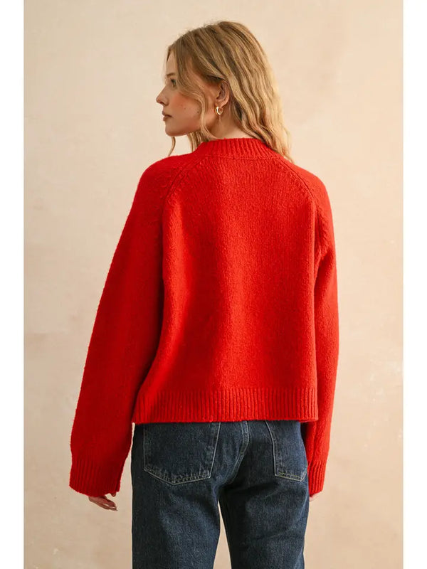 Person wearing a red sweater and blue jeans against a beige background