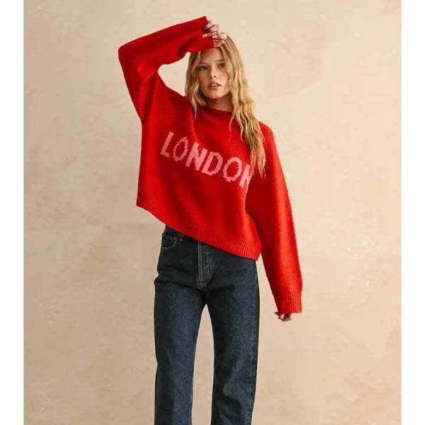 Person wearing a red 'LONDON' sweater and blue jeans against a beige background