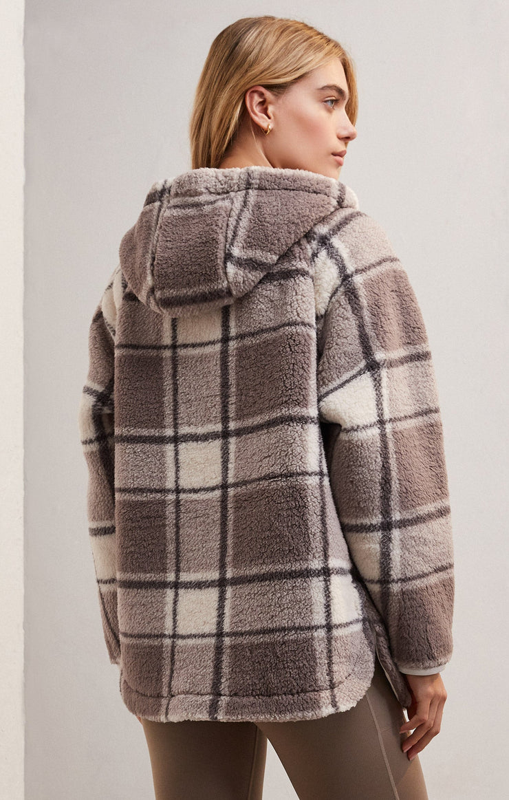 back view of the model wearing the cross country plaid jacket in lunar grey. shows the drawstring hood. also shows the side slits, the plaid print and the oversized, cozy fit.