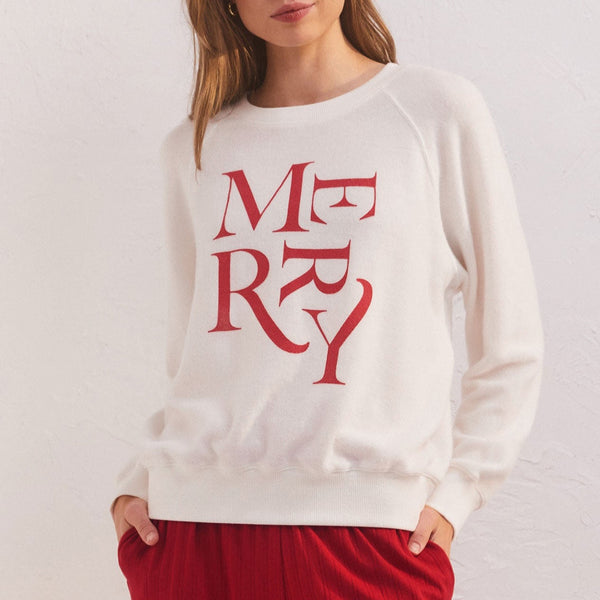 front view of Cassie merry long sleeve top in vanilla ice. shows crew neckline. also shows the defined seams, the merry wording that is in different directions in red, and the tighter band around the bottom and cuffs.