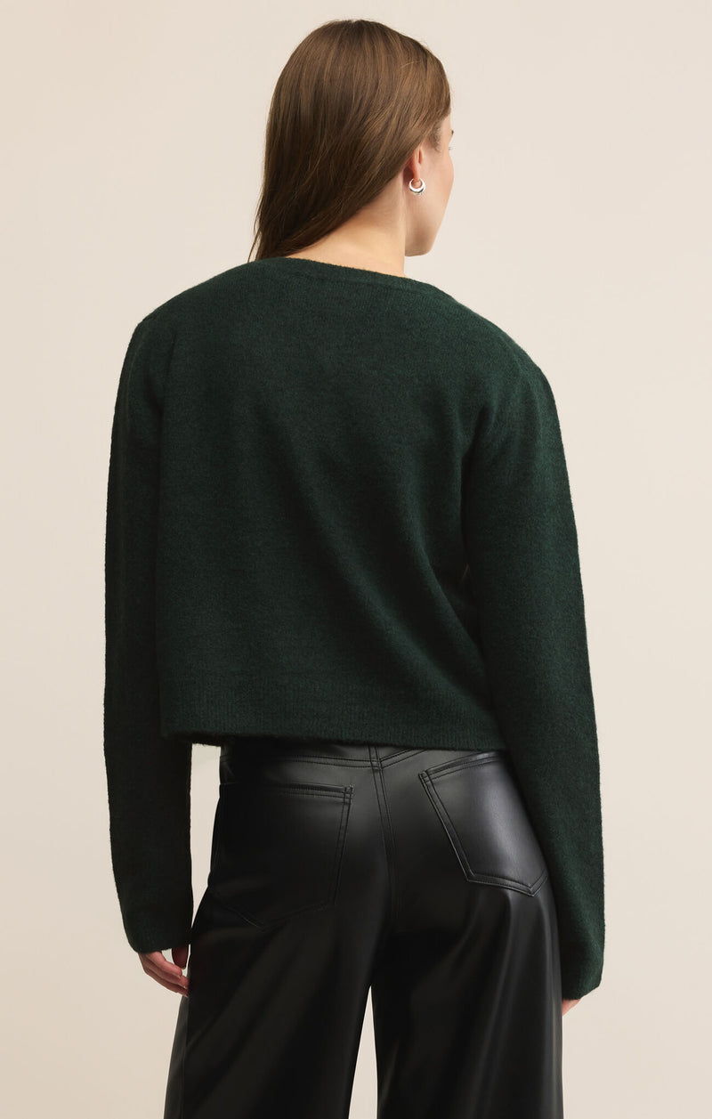 Person wearing a dark green sweater and black pants on a beige background