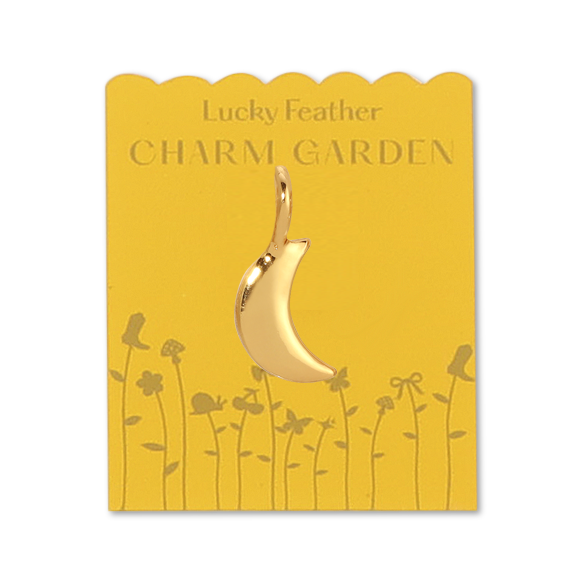 Front view of the gold moon charm on yellow packaging with the gold wording LUCKY FEATHER CHARM GARDEN and gold flowers on the bottom of the packaging. In the middle is the gold moon charm. 