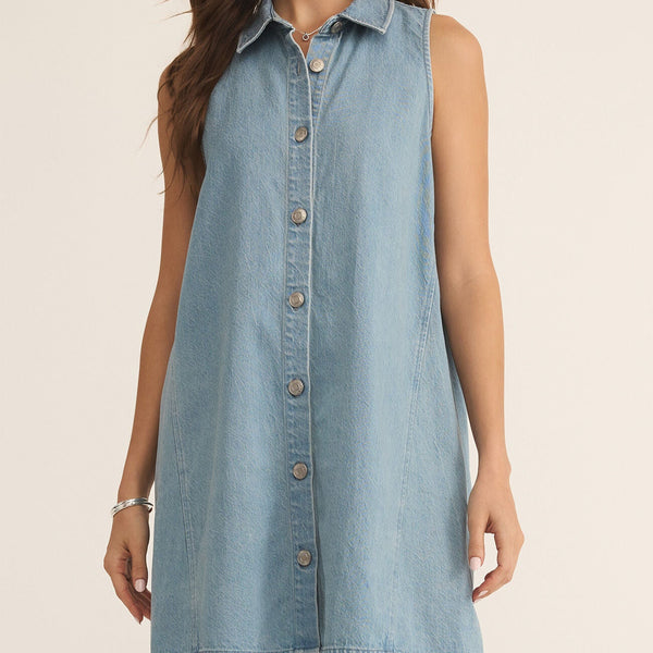 front view of the model wearing the new day twill mini dress. shows the collar. also shows the button down closure, shows the dress is sleeveless and the light wash denim. 