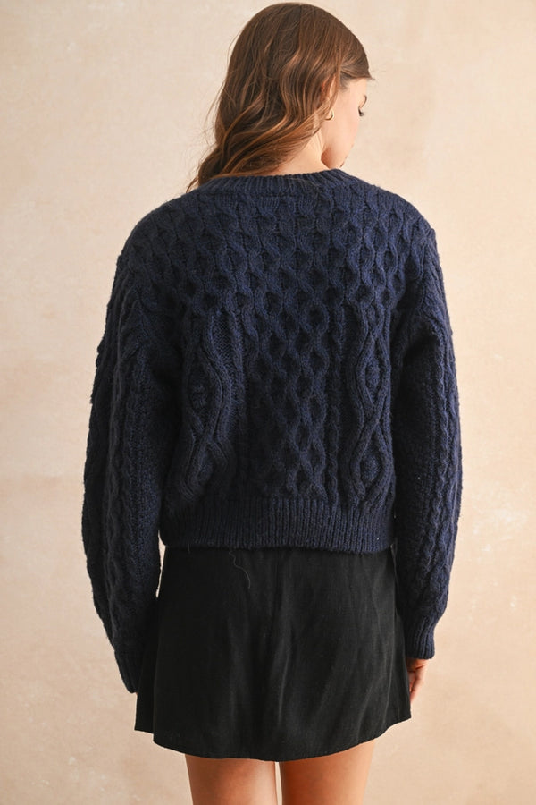 Person wearing a navy blue cable knit sweater against a beige background