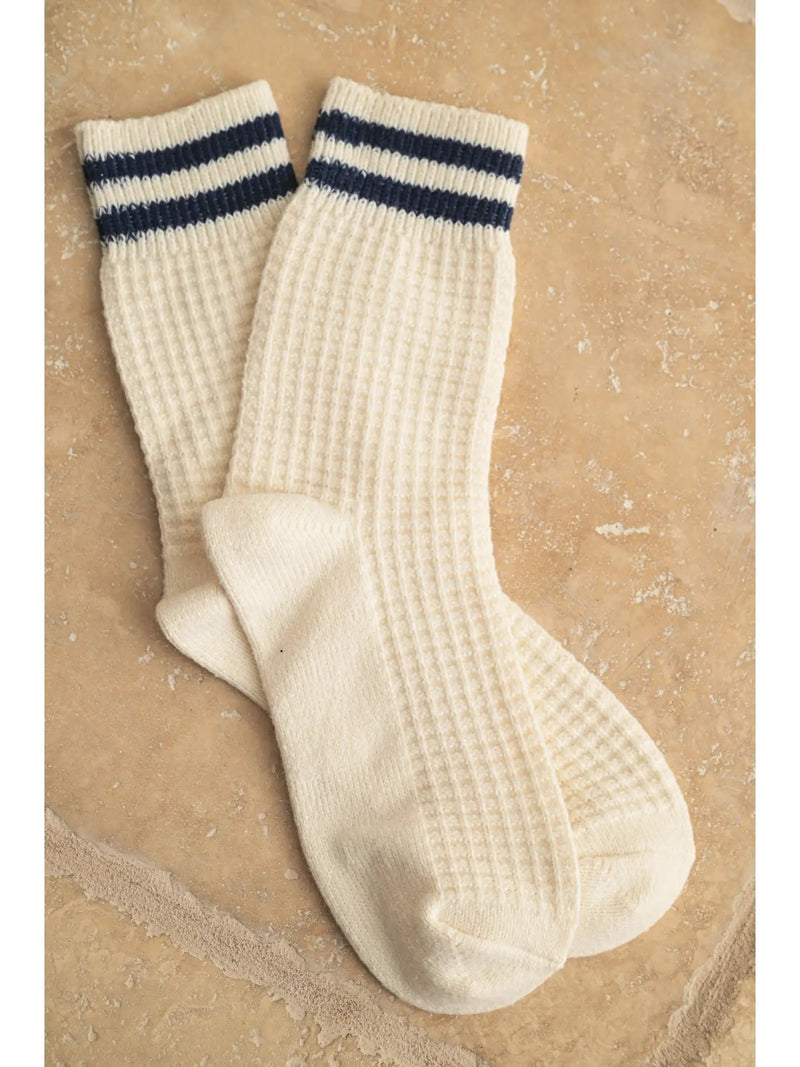 Pair of cream-colored socks with blue stripes on a textured beige background