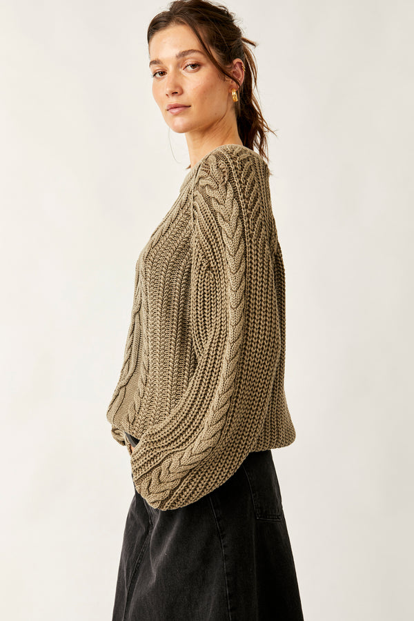 side view of model wearing the Frankie cable sweater in olive stone. shows the scoop neckline. also shows the braided detail on the side go the sleeve and shows the sloucher fir in the body. 