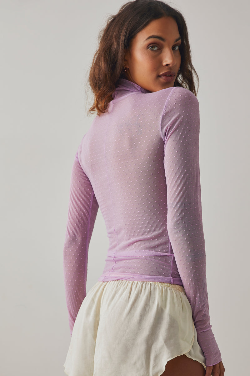 back/side view of model wearing the on the dot layering top in bubble tea. shows the sheer fabric. also shows the exposed seams, the dot detail throughout, the high neckline and the waist length of the top. 