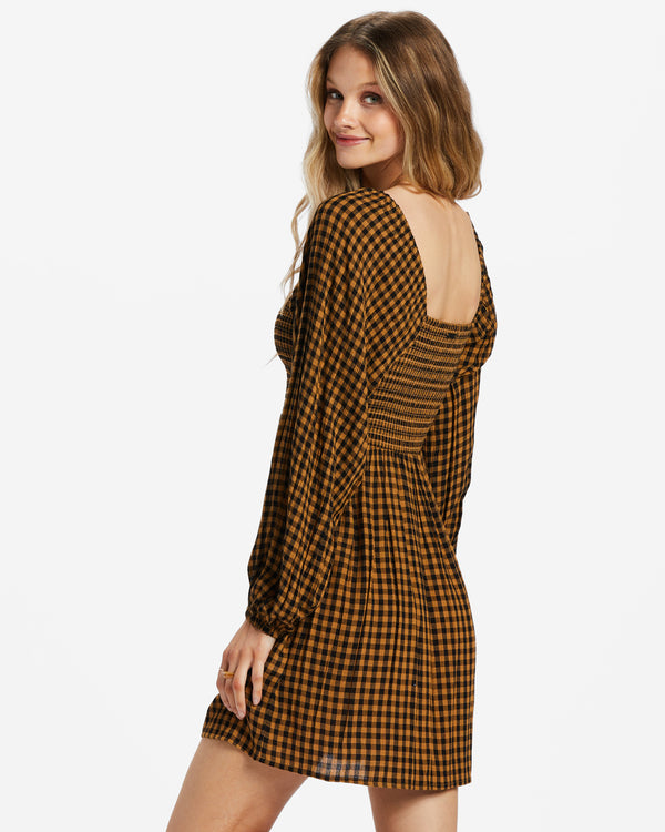 back/side view of model wearing paradise dress. shows the straight neckline with the long puff sleeves, shows the easy fit skirt and the smocked bodice in this brown and black checkered pattern.