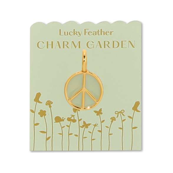 Front view of the gold peace charm on the light green packaging with gold wording LUCKY FEATHER CHARM GARDEN and gold flowers on the bottom. In the middle is the gold peace sign charm with the middle being a sage green color. 
