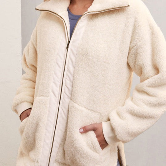 front view of model wearing highest peak jacket in sandstone. shows the oversized collar. also  shows the two way zip up, the two front pockets, the drops shoulders and the plush fabric. 