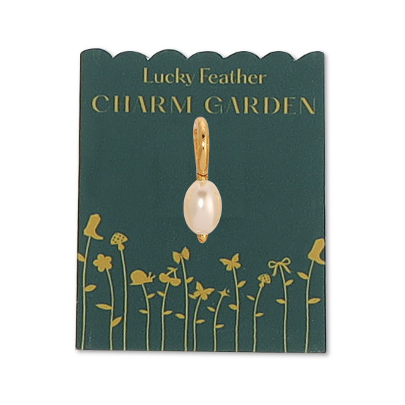 front view of the gold pearl charm on the dark green packaging with gold wording LUCKY FEATHER CHARM GARDEN and at the bottom are gold flowers. The Pearl gold charm is in the middle, the pearl is an oval shape. 
