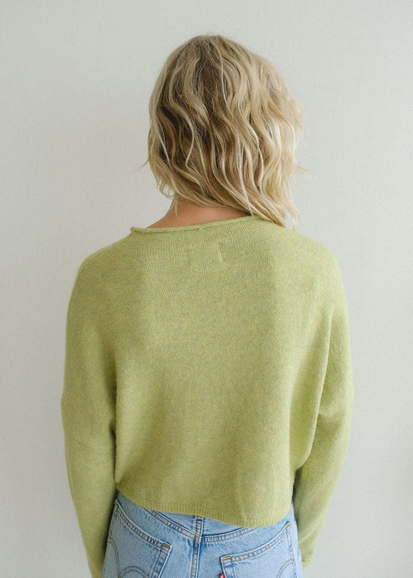 Back view of model wearing cardigan. Shows the waist length. Also shows the rolled hem around the neckline and the cardigan is this beautiful lemongrass green color. 