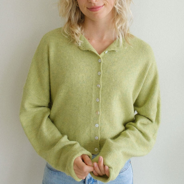 Front view of model wearing cardigan. Shows the button down closure. Also shows the oversized fit and oversized sleeves. also shows that cardigan is waist length. The color of the cardigan is lemongrass, a beautiful green color. 