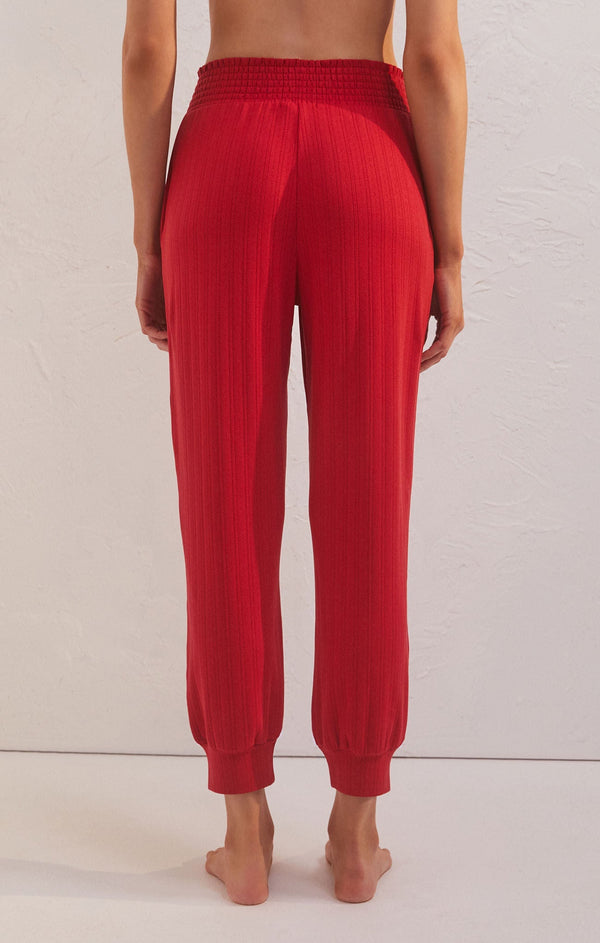 back view of model wearing the holly pointelle jogger in red. shows the tight cuffs at the bottom. also shows the smocked waistband, the ankle length and the ribbed detail throughout. 
