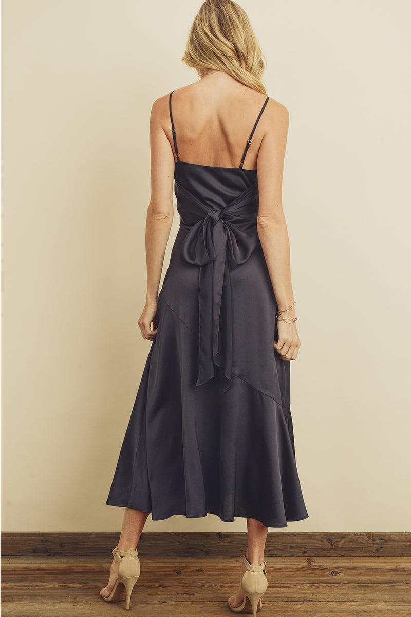 Back view of model wearing dress. Shows the adjustable spaghetti straps. Also shows the tying back sash, the diagonal seaming, flared hem and the color of the dress is navy. 