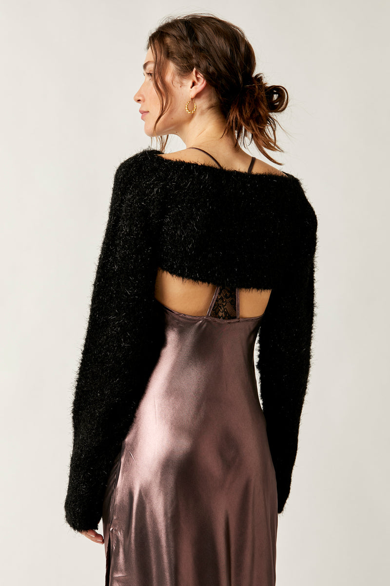 back view of model wearing the shimmer bolero in black. shows the wide neckline from the back. shows the very cropped length of the top and the exaggerated sleeves.