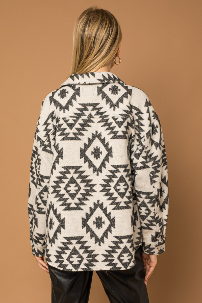 Back view of model wearing shacket. Shows the defined seaming. Also shows the back of the collar and the button on the cuffs. 