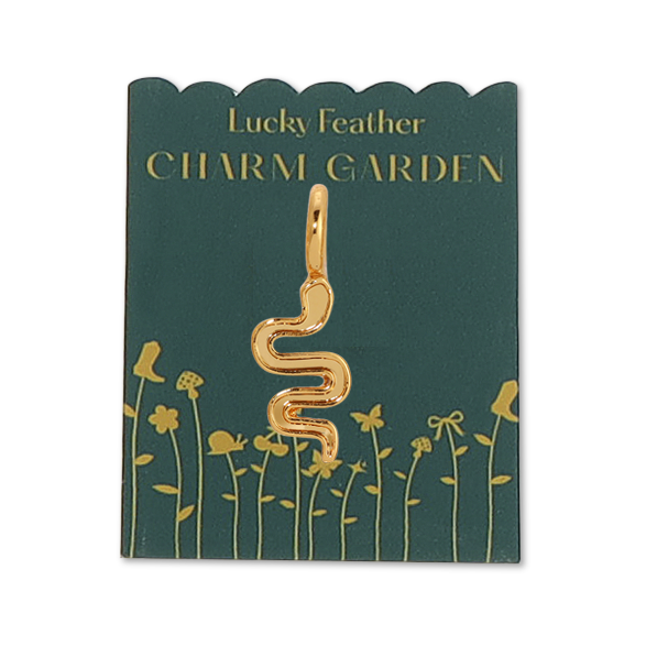 Front view of the gold snake charm on the dark green packaging with the gold wording "LUCKY FEATHER CHARM GARDEN" also with gold flowers. Shows the Gold snake charm in the middle.