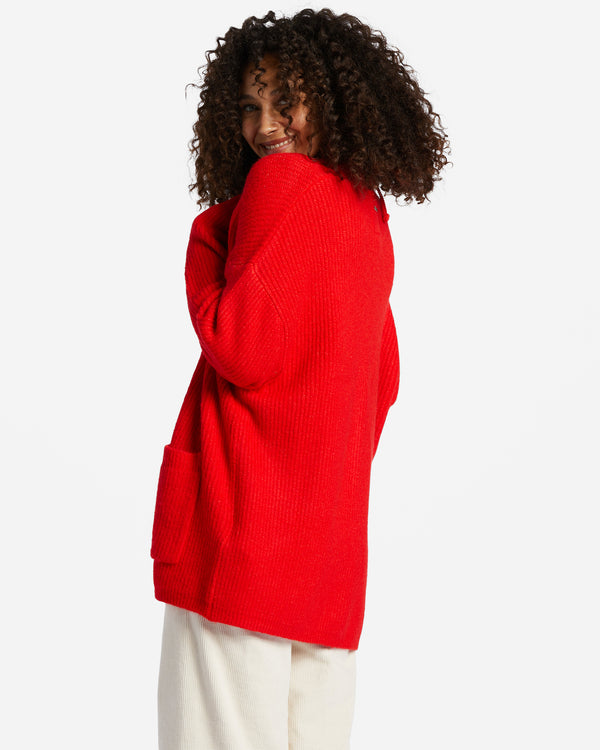 Back/side view of model wearing sweater. Shows the ribbed detail throughout. Also shows the drop shoulder seam, the oversized fit and the rad red color. 