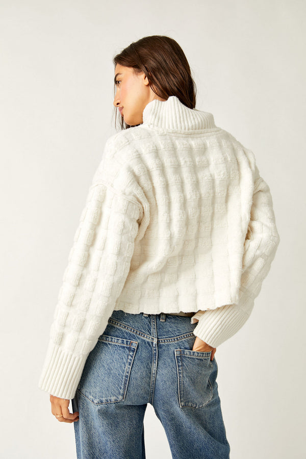 back view of model wearing the soul searcher mock neck sweater in ivory. shows the drop shoulders. also shows the mock neckline, the ribbed hems and the cropped style. 