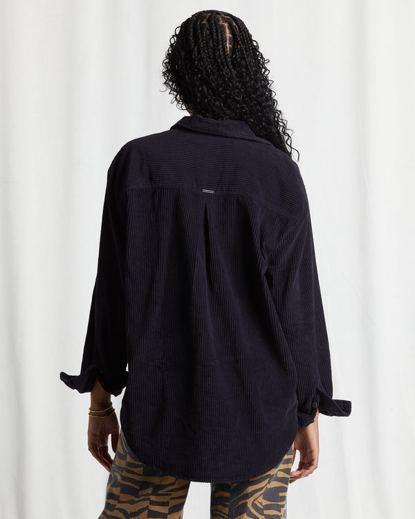 back view of model wearing so stoked top. shows the bottom shirttail hem. the back view of the traditional color, the button closure cuffs, the corduroy material and the black pebble color. 