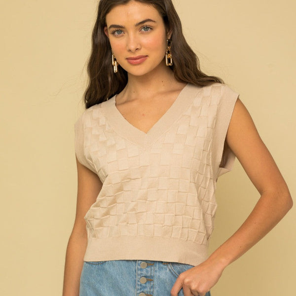 front view of model in the vest. shows the v-neckline, sleeveless design, checkered print, contrast ribbing and oversized fit.