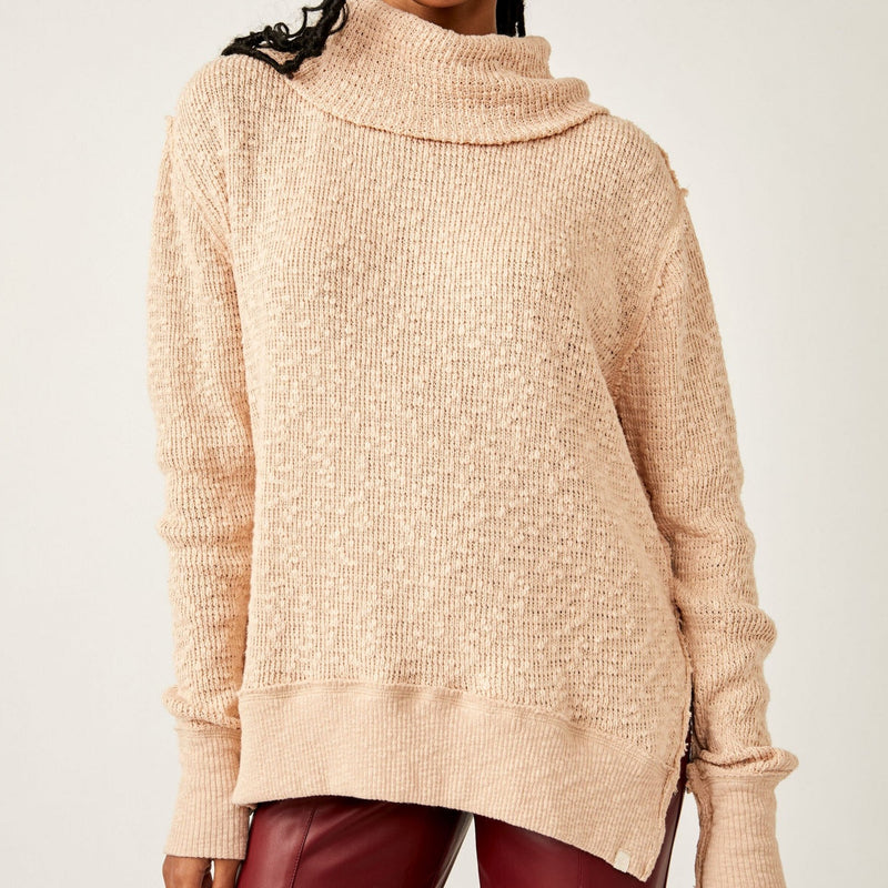 Front view of model wearing turtleneck. Shows dropped shoulders. Also shows the ribbed hems, the slouchy fit and the side slits in this beautiful cream/khaki color. 
