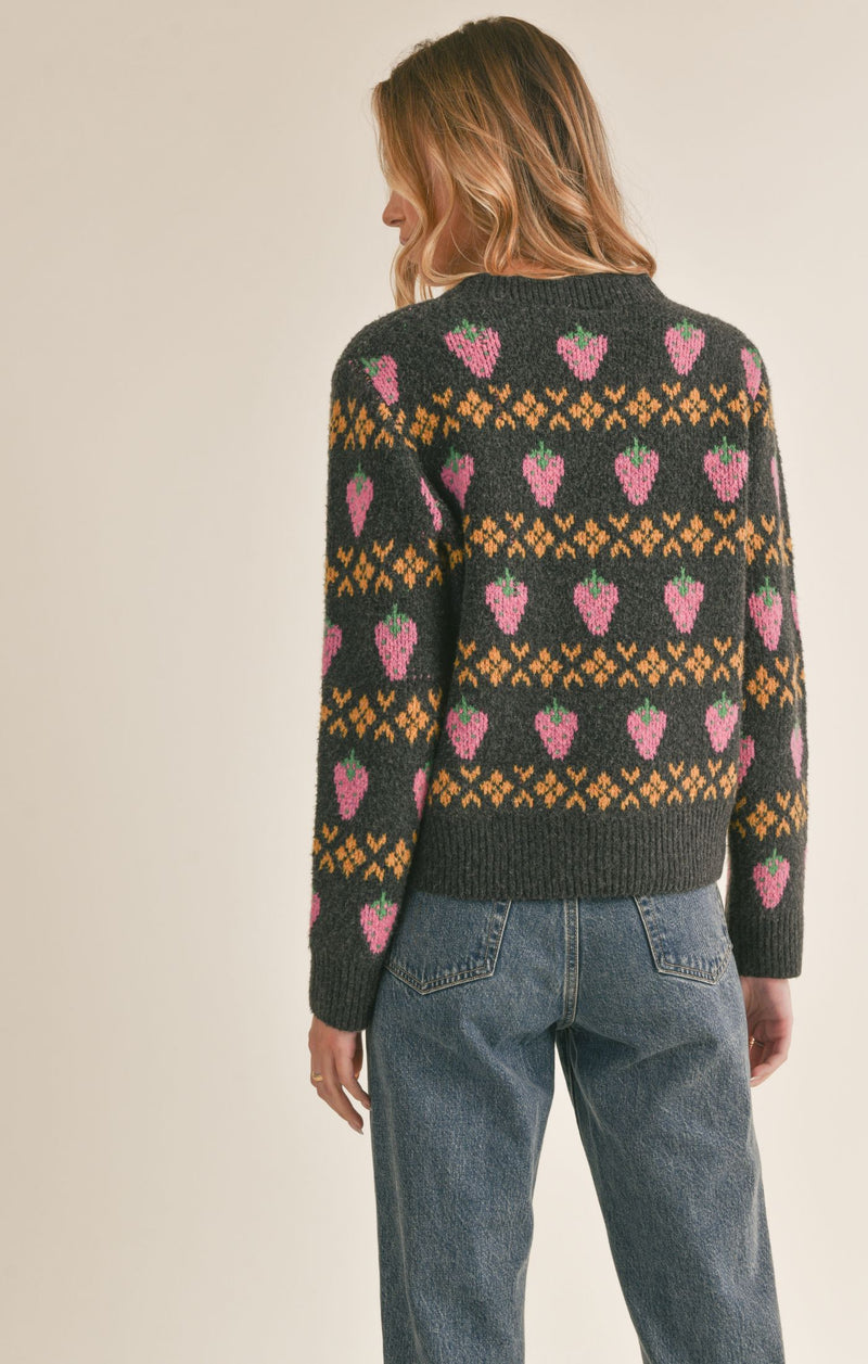 back view of the model wearing the berry sweet sweater. shows the cutest strawberry pattern. also shows the ribbed detail on the neckline, cuffs and bottom hem, and the boxy fit.