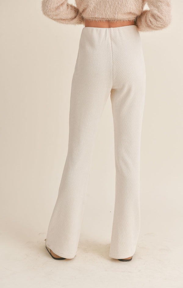 shows the back view of the model wearing the mountain air flair pants in ivory. shows the flare bottoms. also shows the elastic waistband, the pull on style and the high waist. 