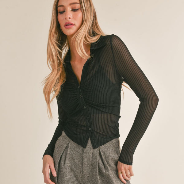 front view of the model wearing the lady dynamite shirt in black. shows the button down closure. also shows the collared neckline, line detailing throughout the sheer fabric and the slim fit and the ruching. 