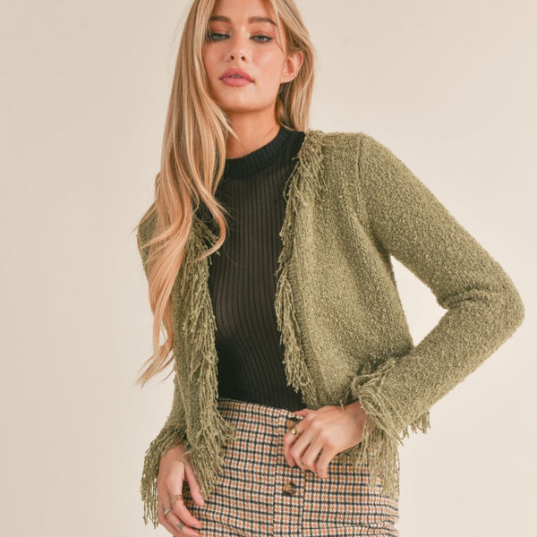 front view of the model wearing the way of being fringe sweater cardigan in olive. shows the fringe detail throughout. also shows the open front and the slim fit.