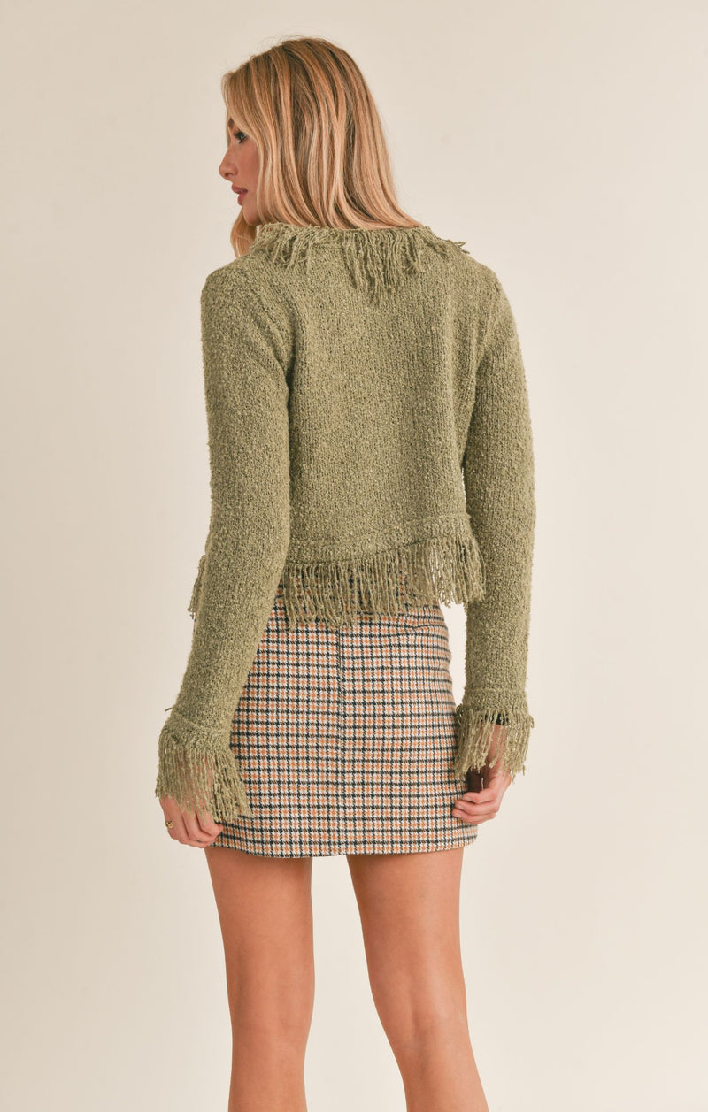 back view of the model wearing the way of being fringed sweater cardigan in olive. shows the fringe detail throughout. also shows the length hits about waist on the model. 
