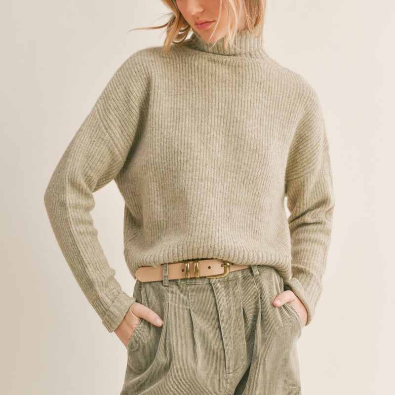 Front view of the model wearing the sweater. Shows the turtleneck neckline. Also shows the drop shoulder hem and the cuff at the sleeve. 