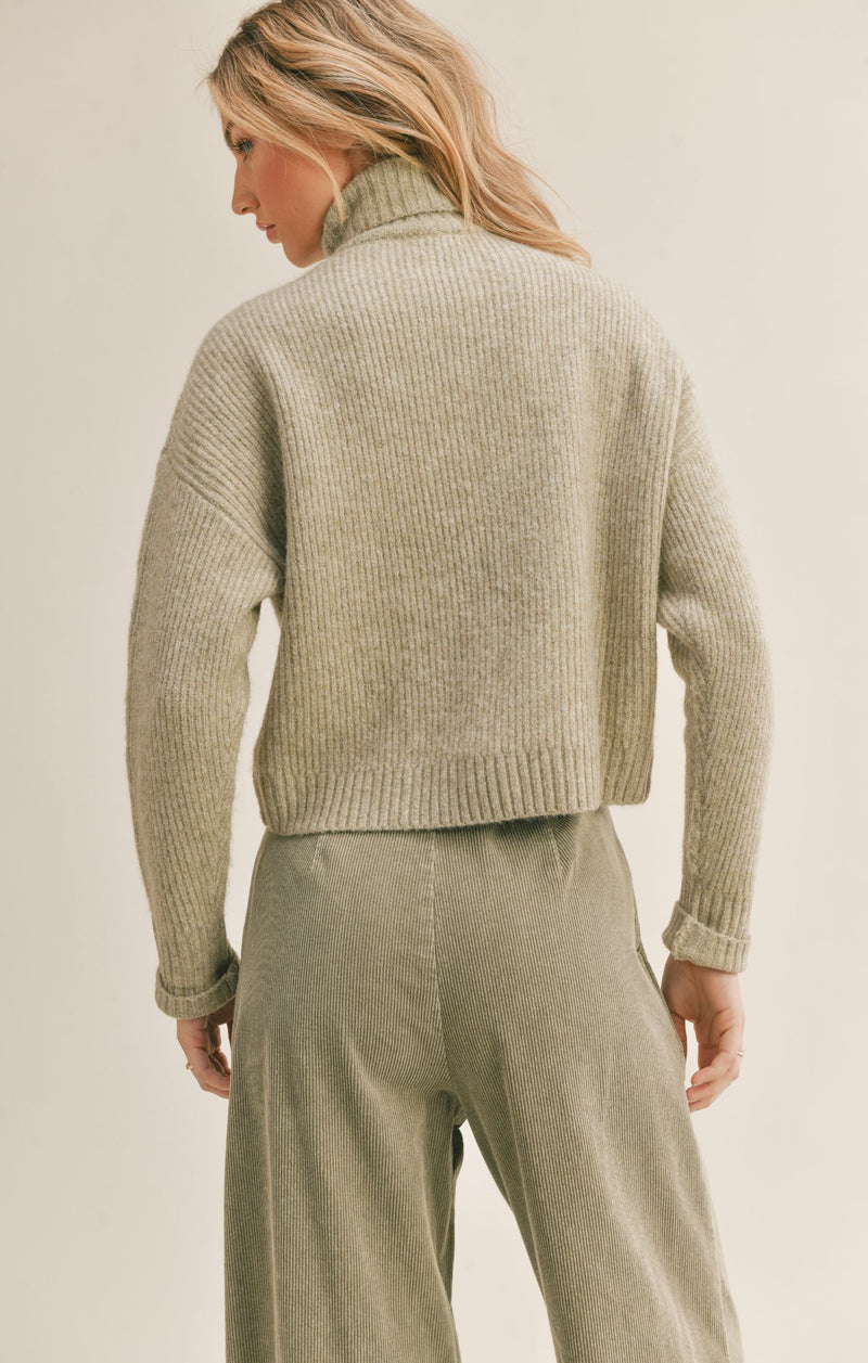 Back view of the sweater. Shows the turtleneck and the drop hem shoulder. Also shows the back is little longer than the front of the sweater. 