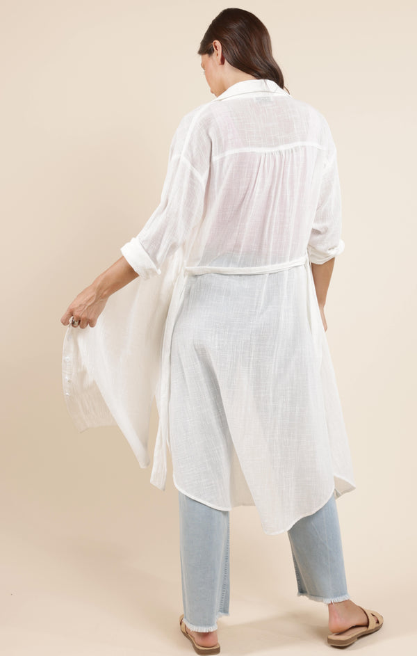 back view of the model wearing the so cal button up duster shirt dress. shows the tie waist. also shows the collar, the sheer materials and the rolled up sleeves. 