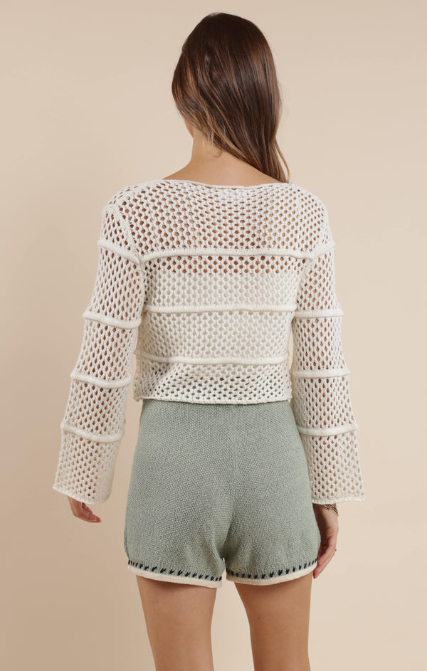 back view of the model wearing the poppy crochet bell sleeve sweater. shows the bell sleeves. also shows the cropped length and the ivory color. 